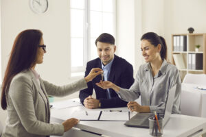 Professional woman sitting behind a desk handing a man and woman house keys